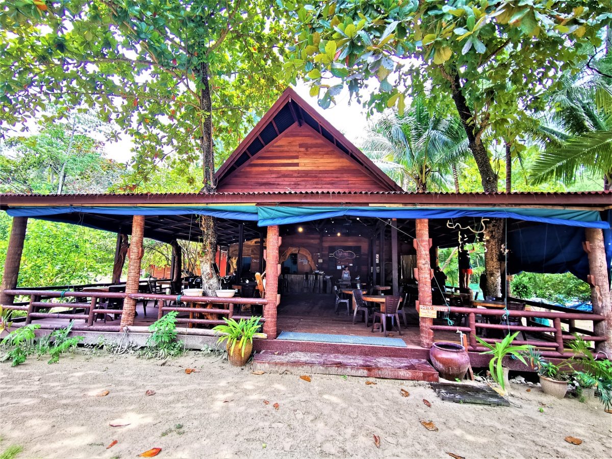 The open-sided timber restaurant at D’Seri Kapas, with tree-trunk posts, long tables and an awning over the deck.
