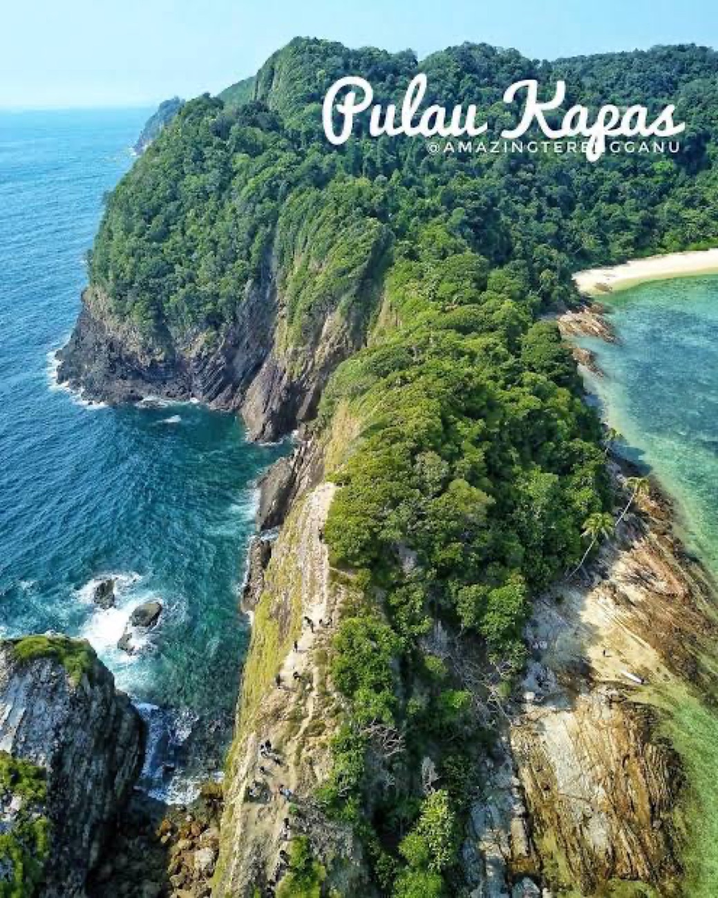 Pulau Kapas from the air: a steep jungled headland dropping into deep blue sea, with a pale sand beach curving away on the sheltered side.