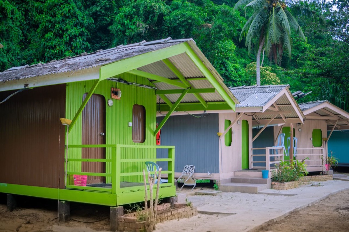 A row of brightly painted timber chalets at Ombak Kapas, lime green and pink with pitched roofs, set against the jungle.